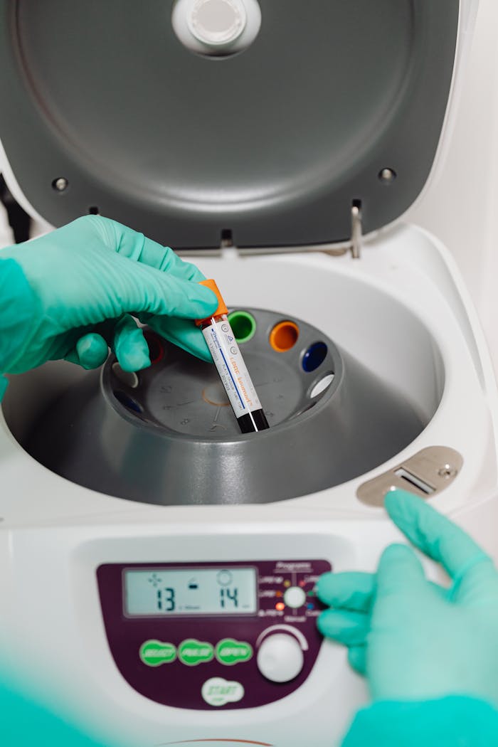 Lab technician operates a centrifuge with a blood sample for testing.